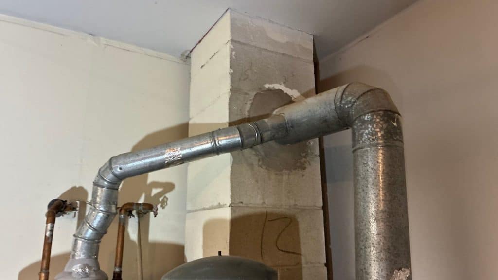 Gas water heater with a metal flue vent pipe running into a chimney in a New Jersey basement